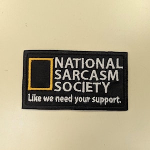 Peut inclure: Écusson rectangulaire noir avec l'inscription blanche "NATIONAL SARCASM SOCIETY". Il comprend un carré jaune et la phrase "Like we need your support." L'écusson est conçu pour être cousu ou repassé sur du tissu.