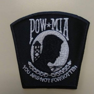 May include: Black embroidered patch with white lettering that reads "POW*MIA You Are Not Forgotten". The patch features a white silhouette of a person's head inside a circle with a barbed wire border.