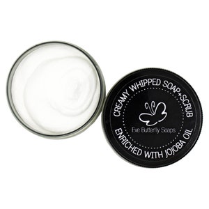 May include: A black jar with a white lid containing a white creamy whipped soap and scrub. The jar has a black label with the text "Creamy Whipped Soap + Scrub Enriched with Jojoba Oil" and a butterfly logo with the text "Eve Butterfly Soaps".
