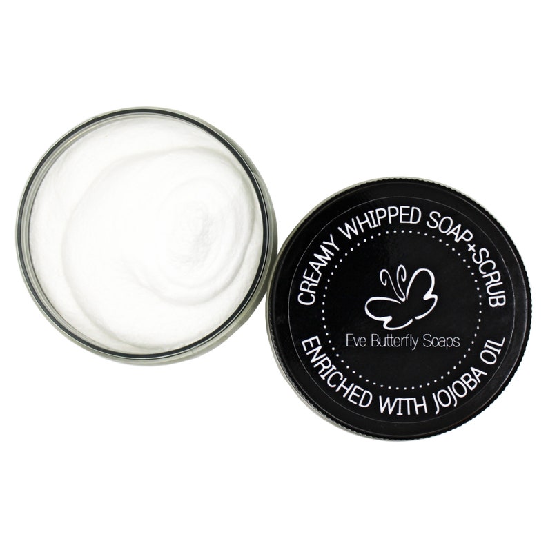 May include: A black jar with a white lid containing a white creamy whipped soap and scrub. The jar has a black label with the text "Creamy Whipped Soap + Scrub Enriched with Jojoba Oil" and a butterfly logo with the text "Eve Butterfly Soaps".