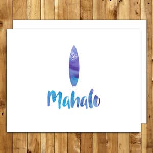 May include: White greeting card with a watercolor design. The card features a blue and purple surfboard with a white flower and the word "Mahalo" in blue watercolor lettering. The card is on a wooden background.