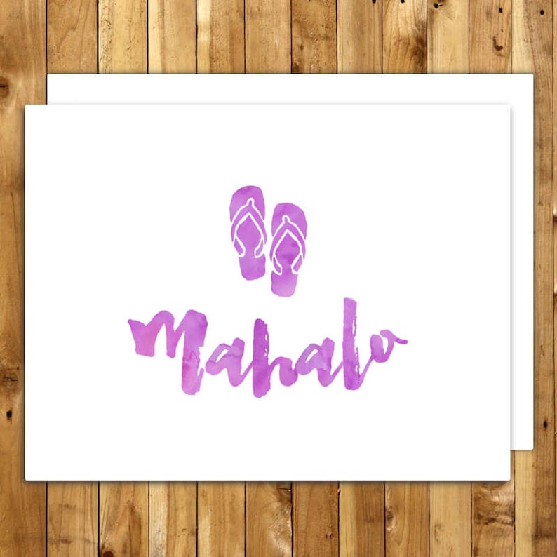 May include: White greeting card with a watercolor design. The card features two purple flip-flops above the word "Mahalo" in purple watercolor lettering. The card is on a wooden background.