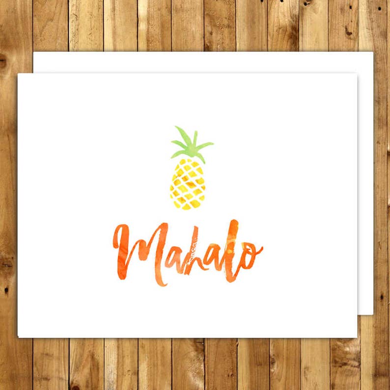May include: White greeting cards with a watercolor pineapple illustration and the word "Mahalo" in orange script. The pineapple is yellow with green leaves. The cards are on a wooden background.