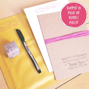 May include: A yellow mailing envelope with a red stamp that says "Kindly Deliver To". A black Sharpie pen and a roll of patterned washi tape are on the envelope. A brown card with the text "You're pretty darn awesome for supporting small business. Thank you. Inanutshellstudio.com" is on top of the envelope. A pink ribbon is on the card. A pink circle with the text "Shipped in rigid or bubble mailer" is in the top right corner of the image.