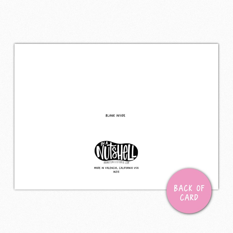 Op de afbeelding: Een witte wenskaart met de tekst "Blank Inside" bovenaan. De kaart heeft een zwart-wit logo met de tekst "In a Nutshell" en de woorden "Back of Card" op een roze cirkel.