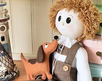 May include: A brown and white stuffed doll with brown hair sits on a wooden surface. The doll is wearing a white shirt, brown overalls, and brown shoes. The doll is holding a brown and orange stuffed dog.