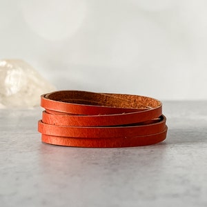 May include: A stack of four brown leather strips, each about 1/2 inch wide, are coiled together. The leather is a rich, reddish-brown color.