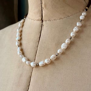 May include: A white pearl necklace with silver accents on a brown fabric background.
