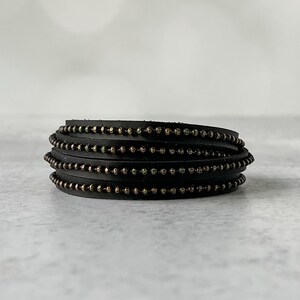 May include: A black leather bracelet with multiple rows of small gold beads.