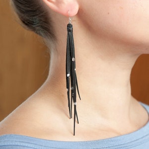 May include: Black leather tassel earrings with silver accents. The earrings are long and dangle from the earlobe.