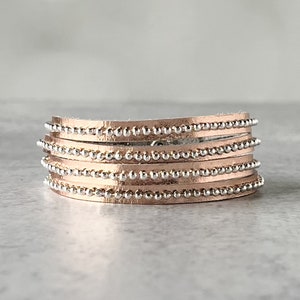 May include: A multi-layered bracelet made of rose gold leather with silver bead accents.