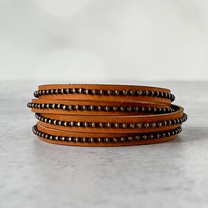 May include: A brown leather bracelet with multiple rows of small gold beads.