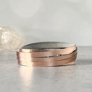 May include: A rose gold leather wrap bracelet with multiple strands of leather. The bracelet is made of a soft, supple leather and has a simple, elegant design.