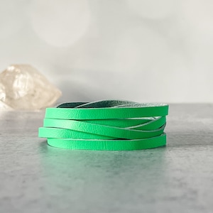 May include: A close-up of a bright green leather cord, folded and stacked on a light gray surface.