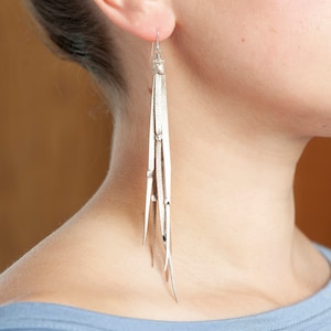 May include: Silver earrings with a long, white leather tassel. The tassel is made of multiple strands of leather that are tied together at the top.