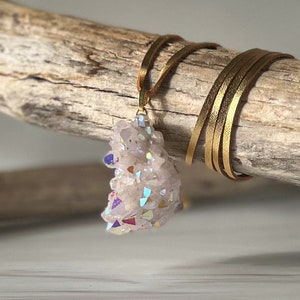 May include: A gold chain necklace with a large iridescent crystal pendant. The crystal is a cluster of many smaller crystals, with a variety of colors, including pink, purple, and blue.