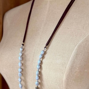 May include: A long necklace with a brown leather cord and a strand of gray pearls. A small brown stone is included in the pearl strand.
