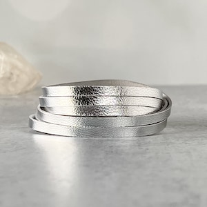 May include: A silver leather wrap bracelet with a textured finish. The bracelet is made of multiple strands of leather that are wrapped around each other.