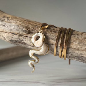 May include: A white snake-shaped pendant necklace with a gold chain. The pendant is made of mother of pearl and has a smooth, polished finish.