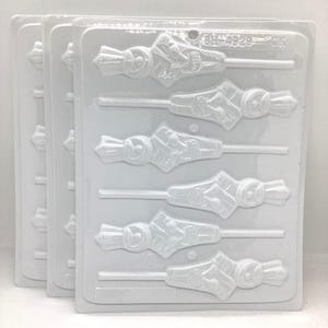 May include: A stack of three white plastic candy molds. Each mold has a series of lollipop-shaped cavities with a design of a crown and a fist. The molds are designed for making candies or chocolates.