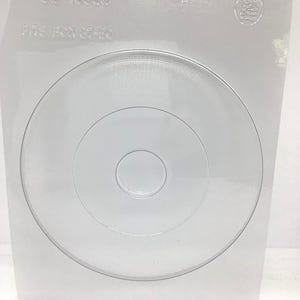 May include: A clear, plastic mold with concentric circular designs. The mold is in a square shape with the text "90-13950" and "FITS BOX 37-80" embossed on the top. A small circular hole is at the top center.