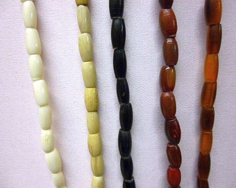 May include: Five strands of beads, each with a different color and material. The beads are oval-shaped and strung on a cord. The colors are white, cream, black, red, and orange.