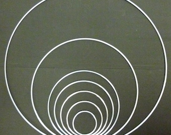 May include: A set of six silver metal hoops of varying sizes, arranged in a concentric pattern on a dark green background.