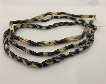 May include: A strand of black and white patterned beads made from bone. The beads are cylindrical and have a twisted design.