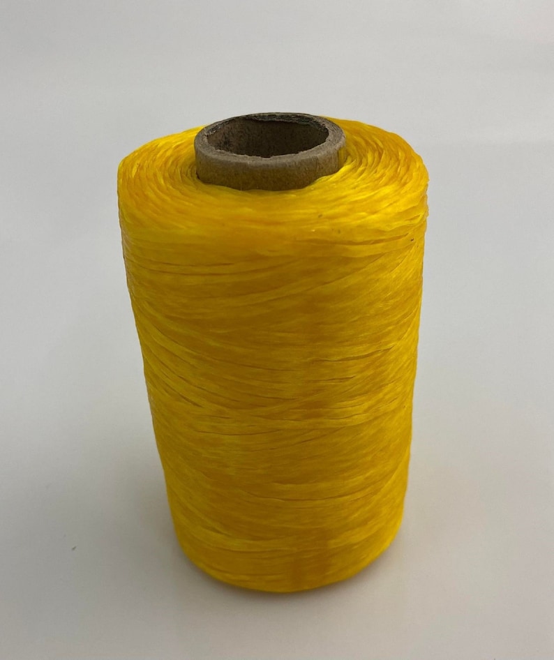 May include: A spool of bright yellow thread wound around a brown cardboard tube.