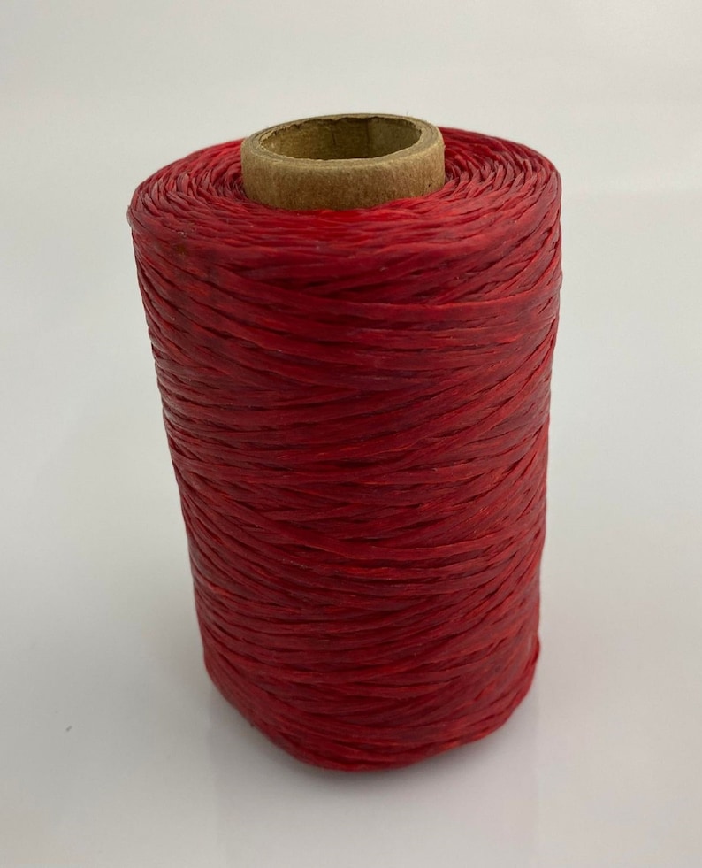 May include: A spool of red waxed linen thread. The thread is wound tightly around a cardboard spool.