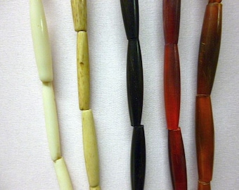 May include: Four strands of beads, each with a different color and material. The beads are cylindrical and strung together. The colors are white, beige, black, and red.