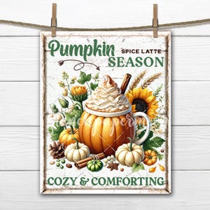 May include: A rectangular sign with the words "Pumpkin Spice Latte Season" and "Cozy & Comforting" in green and white. The image features a pumpkin-shaped mug filled with whipped cream, surrounded by pumpkins, sunflowers, and spices. The sign is hanging from a wooden clothes pin.