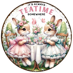 Op de afbeelding: Twee konijnen in roze en blauwe jurken zitten aan een tafel met theekopjes en een theepot. Het bord erboven staat "It's Always Teatime Somewhere".