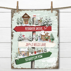 May include: A vintage-style wooden sign with three directional arrows pointing to different Christmas-themed locations: Reindeer Drive, Jingle Bells Lane, and Sugarplum Row. The sign is decorated with snow, houses, and other festive elements.