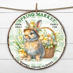 May include: A round, green and white checkered sign with the text "Spring Market" in green letters. The sign features a cartoon bunny wearing a straw hat with baby chicks in a basket. The text "Open Daily", "Family Fun", "Bunnies", "Chicks", and "Flowers" are also on the sign.