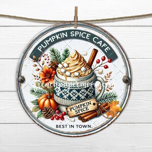 May include: Round metal sign with a distressed white background, featuring a mug of pumpkin spice latte with whipped cream, marshmallows, and a cinnamon stick. The sign includes text that reads "Pumpkin Spice Cafe" and "Best in Town."