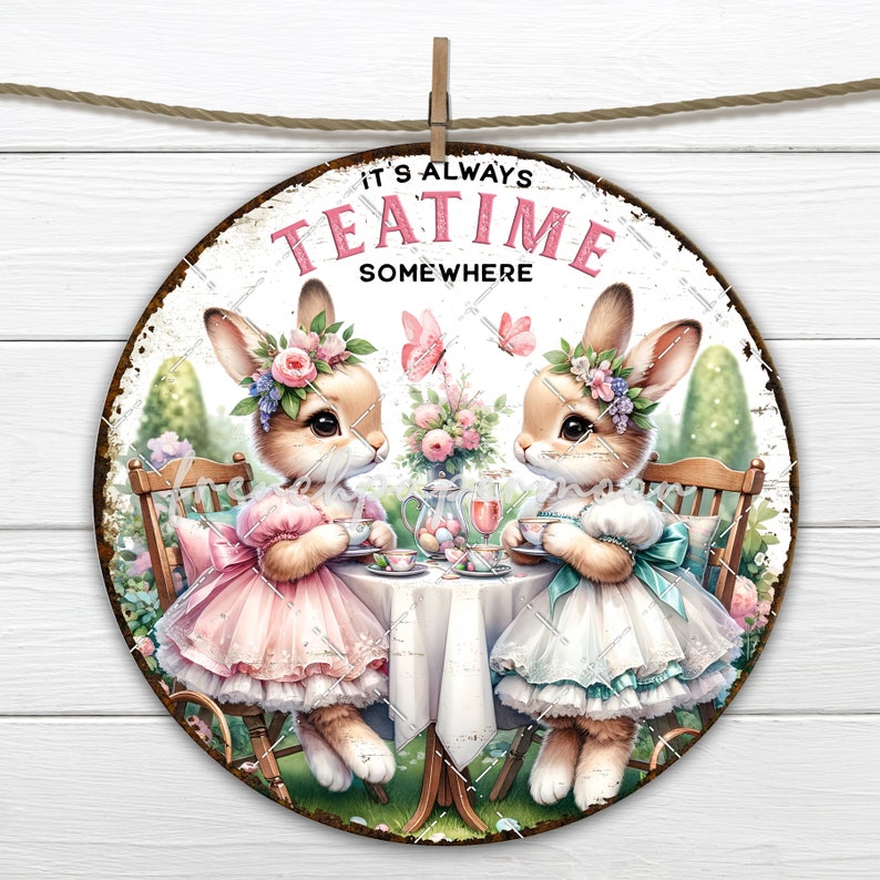 Op de afbeelding: Een rond metalen bord met een witte achtergrond en een verweerde look. Het toont twee konijnen die bloemenkransen en jurken dragen, zittend aan een tafel met theekopjes en een theepot. Het bord zegt "It's Always Teatime Somewhere".