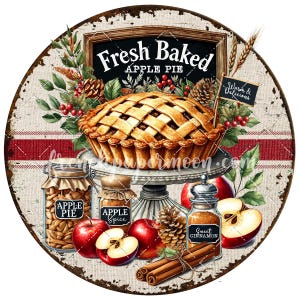 May include: A rustic round sign with a distressed metal finish featuring a freshly baked apple pie on a white pedestal. The sign also includes jars of apple pie and apple spice, a jar of cinnamon, and red apples. The sign reads "Fresh Baked Apple Pie" and "Warm & Delicious".