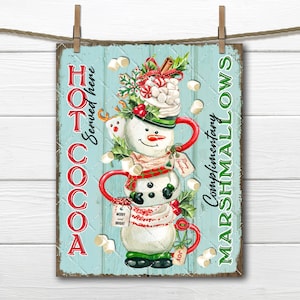 May include: A blue and white sign with a snowman made of mugs of hot cocoa. The sign says "Hot Cocoa Served Here" and "Complimentary Marshmallows".