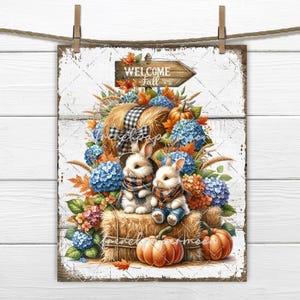 May include: A white wooden sign with a welcome fall sign and two bunnies sitting on a bale of hay with pumpkins and autumnal flowers.