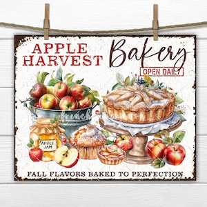 May include: A vintage-style metal sign with a white background and red text that reads "Apple Harvest Bakery Open Daily". The sign features a watercolor illustration of a basket of apples, a jar of apple jam, a pie, and two muffins. The text "Fall Flavors Baked to Perfection" is at the bottom of the sign.