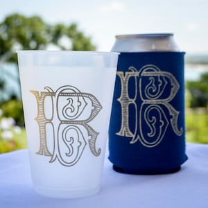 May include: Two white plastic cups with a silver monogram of the letter "R" on them. One cup is a standard cup and the other is a can cooler with a navy blue exterior.