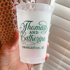 May include: A translucent frosted plastic cup featuring dark green printed text that reads Thomas AND Catherine and CHARLESTON, SC. The cup has a tapered cylindrical shape with a smooth rim and a slightly wider top than the base.