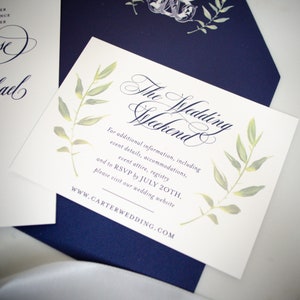 May include: White card with navy blue text and green watercolor leaves. The text reads "The Wedding Weekend" and includes information about additional details, accommodations, event attire, registry, and RSVP by July 20th. The website address is WWW.CARTERWEDDING.COM.