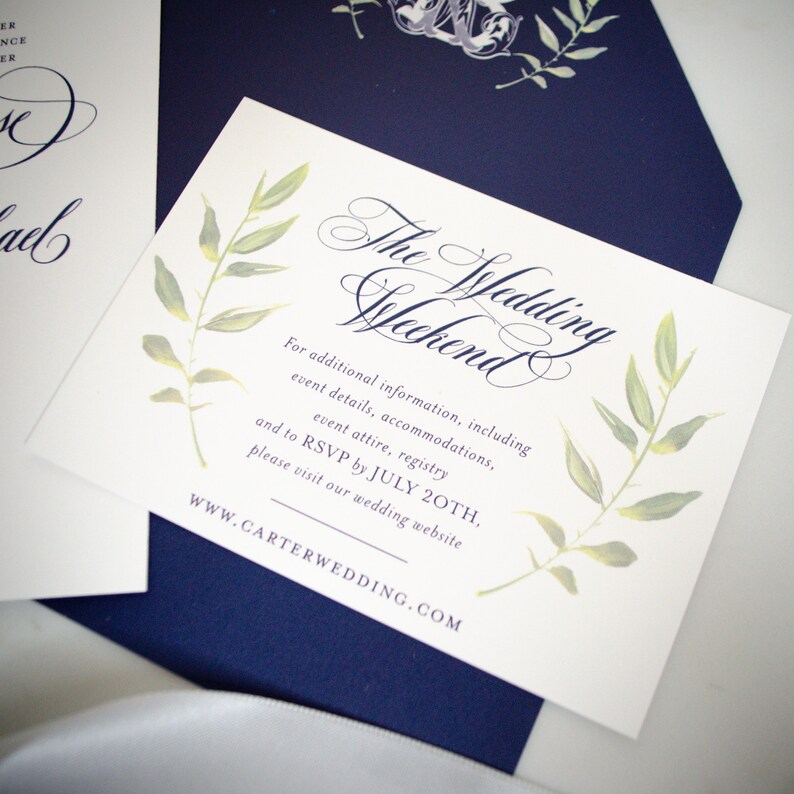 May include: White card with navy blue text and green watercolor leaves. The text reads "The Wedding Weekend" and includes information about additional details, accommodations, event attire, registry, and RSVP by July 20th. The website address is WWW.CARTERWEDDING.COM.