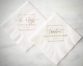 May include: Two square white paper napkins featuring metallic foil printing. One napkin displays the name Buckley, Marie & Grant, and 11.17.18 in rose gold. The other displays Lambert, David & Grace Anne, and 12.15.18 in gold foil.