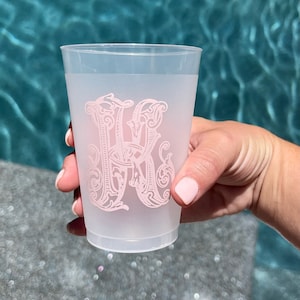 May include: A frosted plastic cup with a pink monogram of the letter "K" in a decorative font.