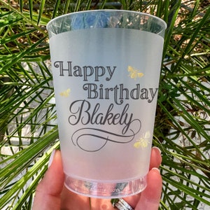 May include: A frosted plastic cup with a black and white design that says "Happy Birthday Blakely" with gold bee accents.