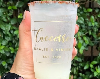 May include: A frosted plastic cup with a chili-salt rim and a black straw, featuring gold text that reads "Cucerra", "NATALIE & VINCENT", and "EST 2020" inside a thin gold rectangular border, containing a pale yellow liquid with visible ice cubes.