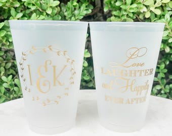 May include: Two frosted plastic cups featuring gold lettering. One cup displays the initials I & K inside a circular leaf wreath. The other cup features the text Love LAUGHTER and Happily EVER AFTER in a mix of script and block fonts.